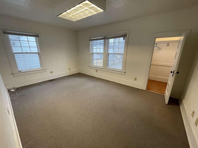 unfurnished bedroom featuring a spacious closet, baseboards, dark colored carpet, and a closet