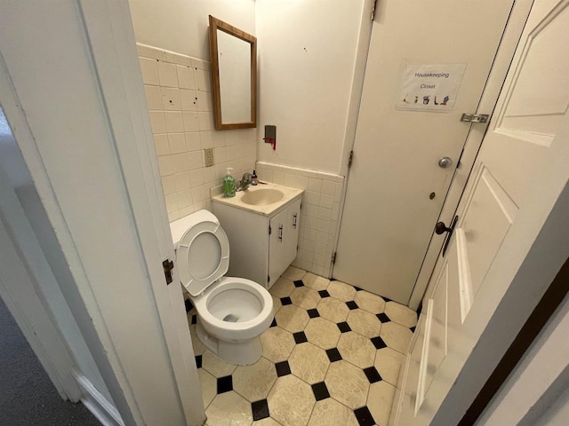 bathroom featuring toilet, a wainscoted wall, vanity, and tile walls