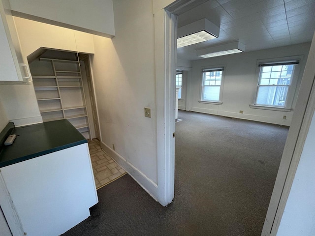 hallway with baseboards and dark carpet