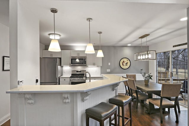 kitchen with a breakfast bar area, stainless steel appliances, light countertops, decorative backsplash, and dark wood-type flooring