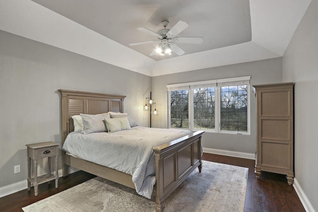 bedroom featuring a ceiling fan, a tray ceiling, dark wood-style flooring, and baseboards