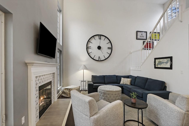 living area with stairs, a high ceiling, wood finished floors, and a tile fireplace