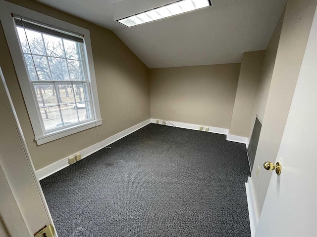 additional living space with dark colored carpet, vaulted ceiling, and baseboards