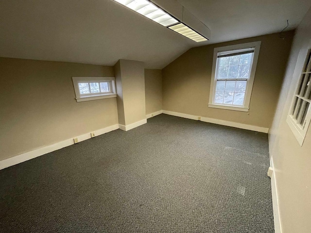 bonus room featuring lofted ceiling, visible vents, dark carpet, and baseboards