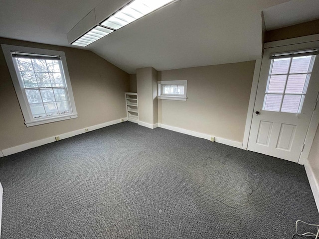 additional living space with lofted ceiling, a healthy amount of sunlight, carpet flooring, and baseboards