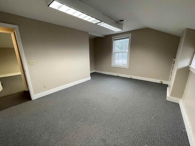 additional living space with dark colored carpet, visible vents, vaulted ceiling, and baseboards