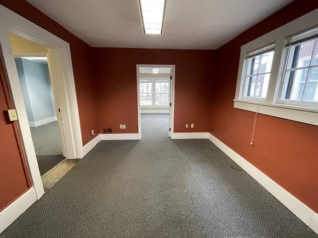 spare room with plenty of natural light, baseboards, and dark colored carpet