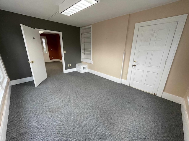 empty room featuring dark colored carpet and baseboards