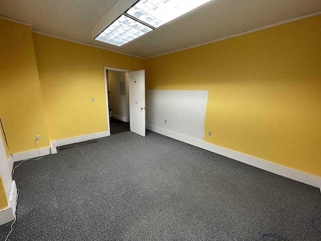 empty room featuring ornamental molding, dark carpet, and baseboards