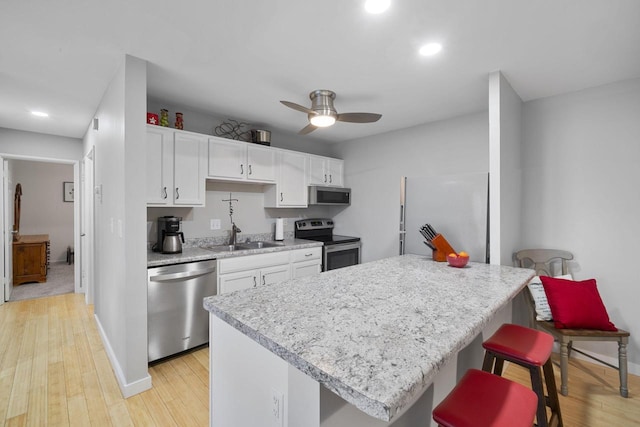 kitchen featuring stainless steel appliances, white cabinets, ceiling fan, light wood-type flooring, and a kitchen breakfast bar