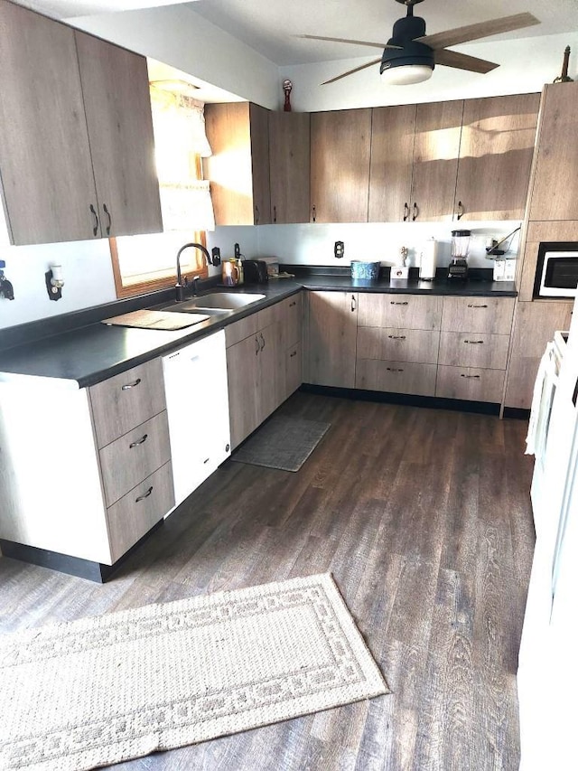 kitchen with ceiling fan, white appliances, a sink, dark countertops, and dark wood finished floors