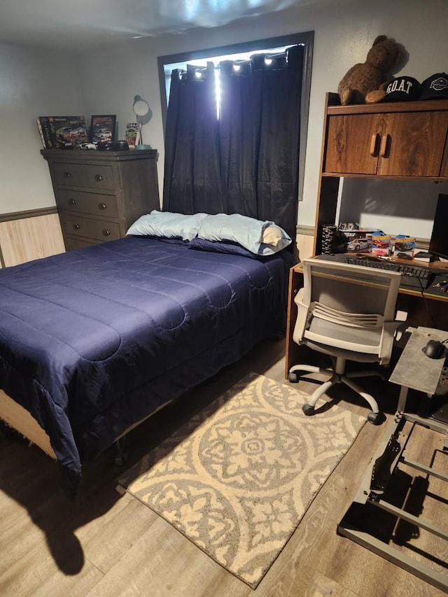 bedroom featuring a wainscoted wall and wood finished floors