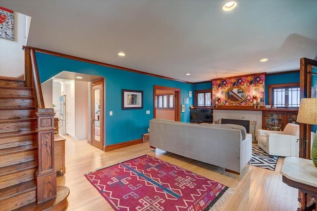 living area featuring recessed lighting, light wood-style floors, stairs, ornamental molding, and a brick fireplace