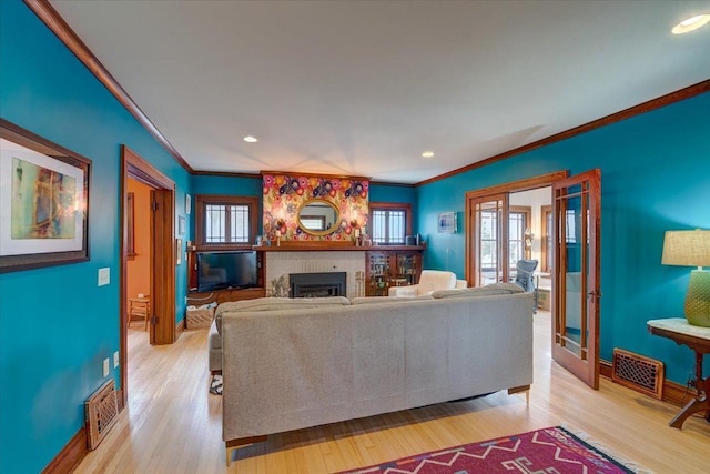 living room with a fireplace, baseboards, french doors, ornamental molding, and light wood finished floors