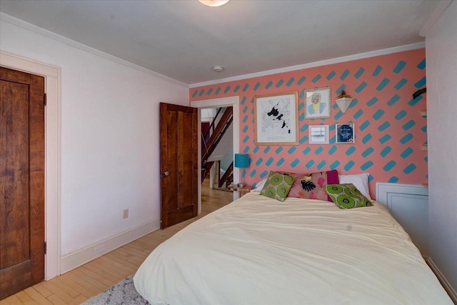 bedroom featuring an accent wall, baseboards, light wood-style floors, ornamental molding, and wallpapered walls