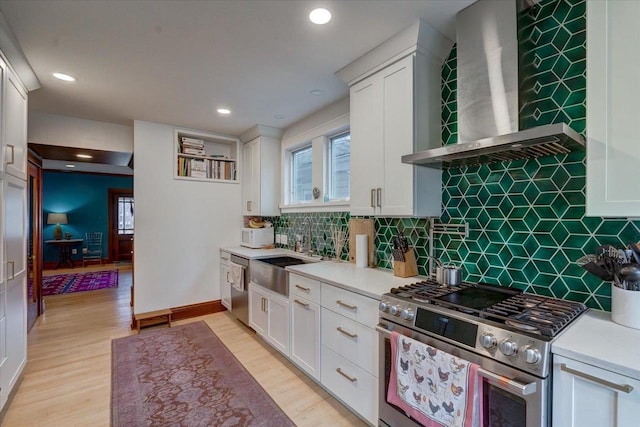 kitchen with appliances with stainless steel finishes, a sink, wall chimney range hood, and light wood finished floors