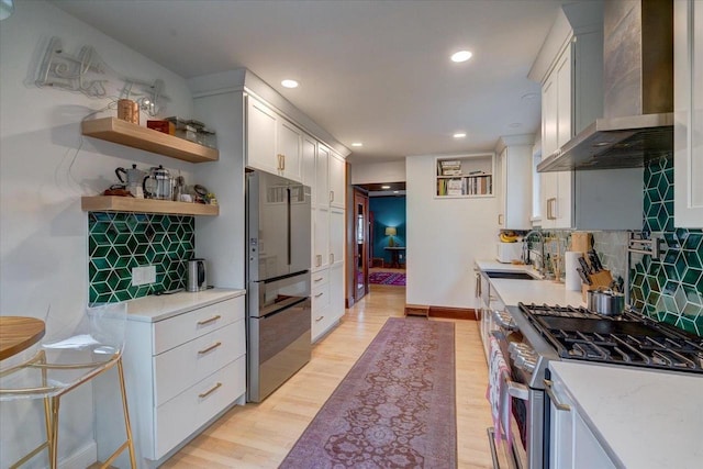 kitchen featuring stainless steel appliances, wall chimney range hood, light wood-style flooring, and decorative backsplash