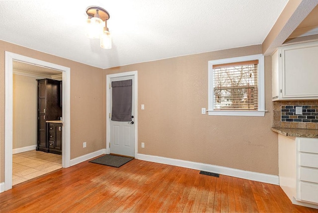 unfurnished dining area with light wood-style floors, a textured ceiling, and baseboards