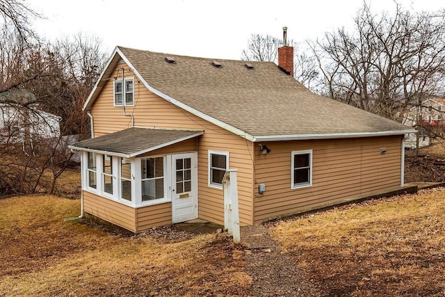 rear view of house featuring a sunroom, a chimney, and roof with shingles