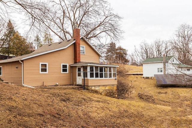 rear view of property featuring a sunroom and a chimney