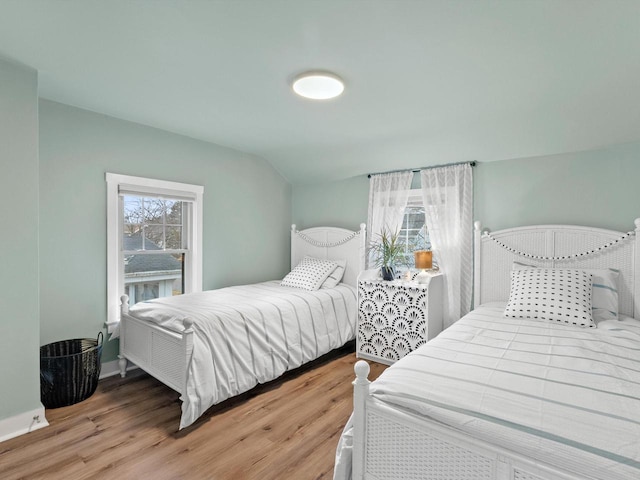 bedroom with multiple windows, baseboards, vaulted ceiling, and wood finished floors