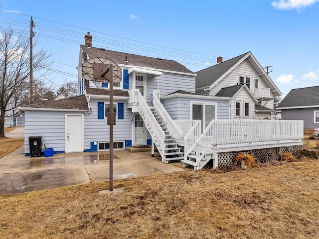 rear view of property featuring roof with shingles, a chimney, and a wooden deck