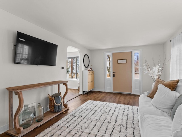 living room featuring baseboards, arched walkways, and wood finished floors