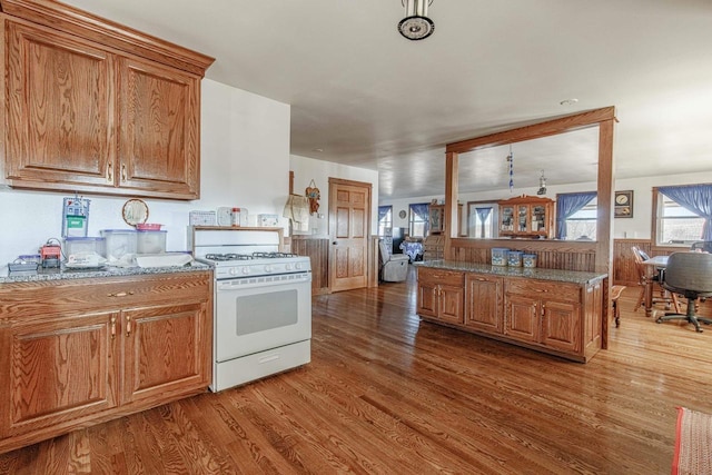 kitchen with light stone counters, brown cabinetry, wood finished floors, and white range with gas stovetop