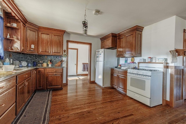 kitchen featuring white appliances, dark wood-style floors, light stone counters, brown cabinets, and backsplash