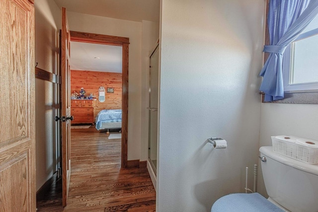 bathroom featuring wood walls, a shower stall, toilet, and wood finished floors