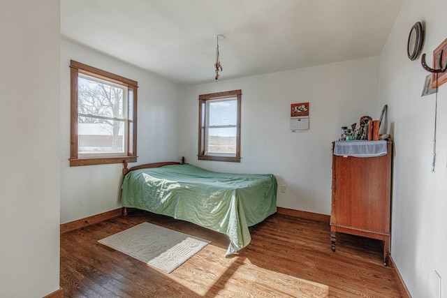 bedroom with multiple windows, baseboards, and wood finished floors