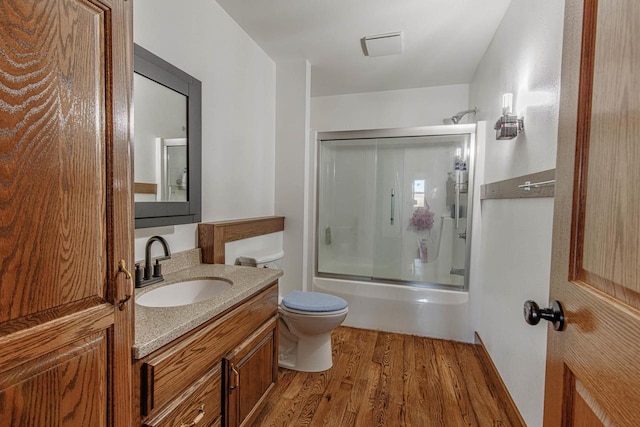 bathroom featuring toilet, combined bath / shower with glass door, wood finished floors, and vanity