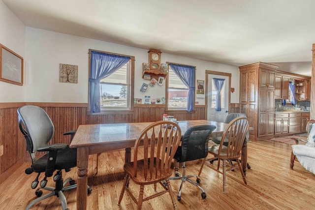 dining space featuring light wood-style flooring, wooden walls, and wainscoting