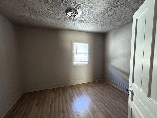 unfurnished room with a textured ceiling, baseboards, and wood finished floors