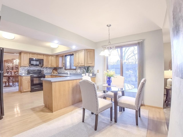 kitchen with a peninsula, an inviting chandelier, light brown cabinetry, black appliances, and backsplash