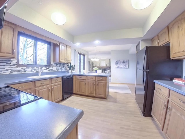 kitchen featuring light wood-style flooring, a peninsula, a sink, black appliances, and backsplash