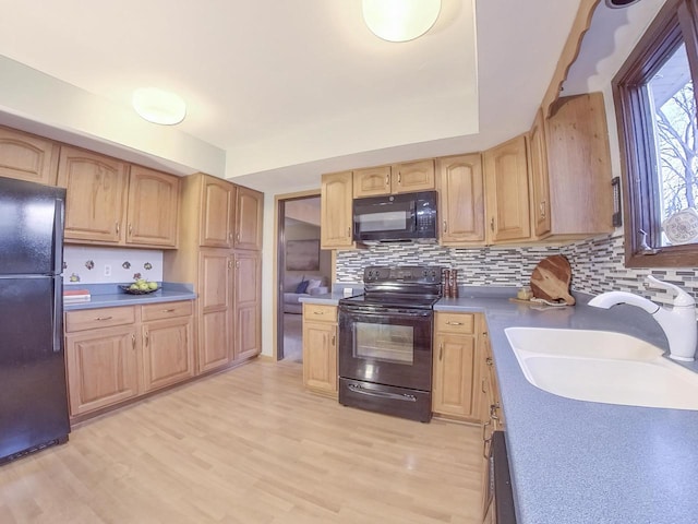 kitchen featuring light brown cabinets, a sink, light wood finished floors, and black appliances