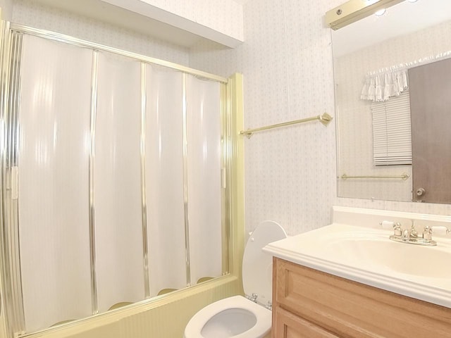 bathroom featuring enclosed tub / shower combo, vanity, toilet, and wallpapered walls