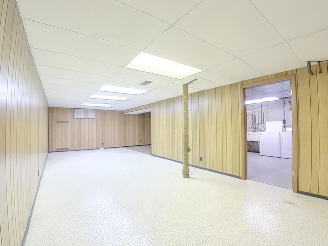 finished below grade area featuring a paneled ceiling, wood walls, and independent washer and dryer