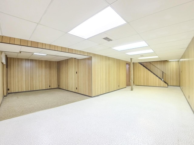 finished below grade area with wooden walls, visible vents, light carpet, and a drop ceiling