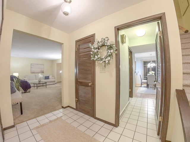 hallway with light carpet, light tile patterned floors, baseboards, and stairway