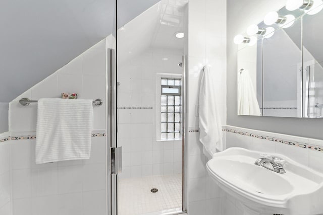 bathroom with a sink, tile walls, a shower stall, and vaulted ceiling