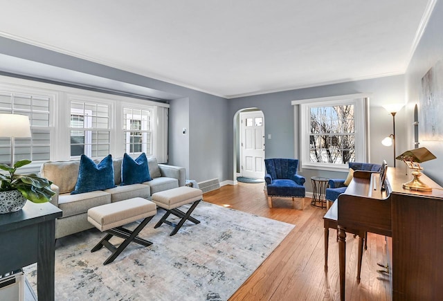 living area with hardwood / wood-style flooring, crown molding, a healthy amount of sunlight, and arched walkways