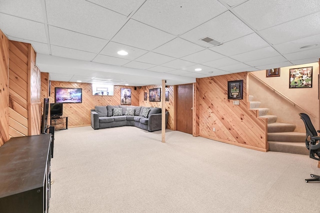 living room with visible vents, carpet floors, wood walls, and stairway