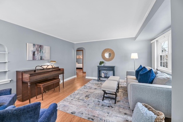 living area featuring baseboards, arched walkways, wood finished floors, and ornamental molding