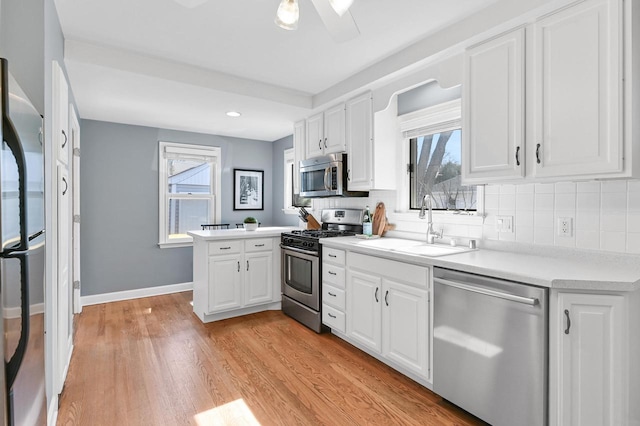 kitchen with light wood-style flooring, a sink, appliances with stainless steel finishes, a peninsula, and white cabinets