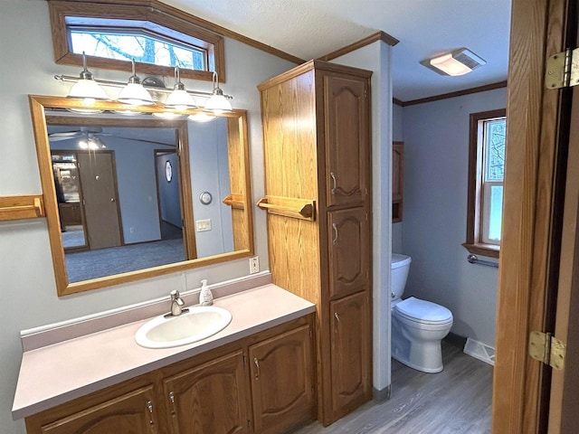 bathroom featuring toilet, ornamental molding, wood finished floors, and vanity