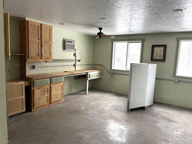 kitchen with brown cabinetry, ceiling fan, a wall mounted air conditioner, a textured ceiling, and concrete floors