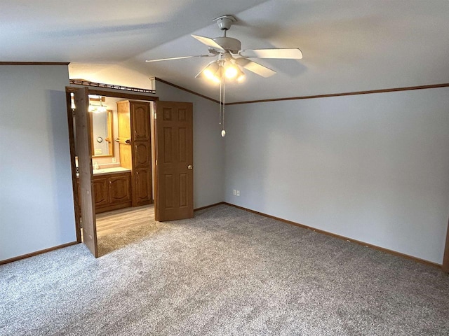 unfurnished bedroom featuring light carpet, baseboards, lofted ceiling, ensuite bathroom, and crown molding