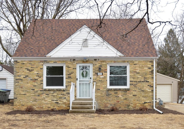 view of front of property featuring entry steps, a garage, an outbuilding, roof with shingles, and brick siding